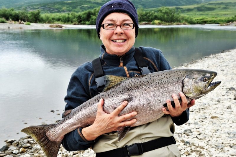 Alaskan King Salmon: An eager angler smiles while holding a large Alaskan king salmon on the shoreline.